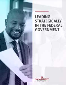 One man in a suit and tie looking at a piece of paper held by another person next to the title "Leading Strategically in the Federal Government."